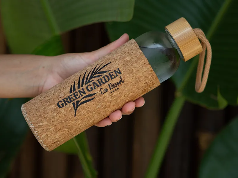 Hand holding a cork-wrapped bottle labeled "Green Garden Eco Resort."