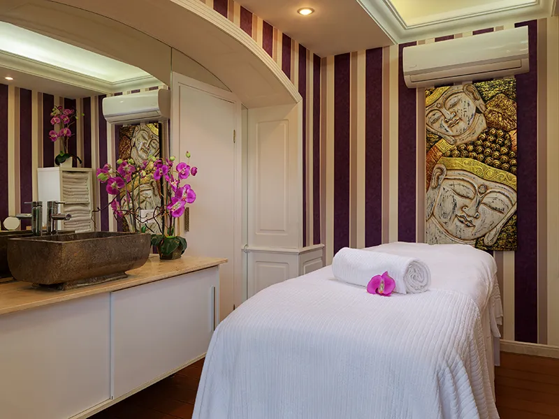 Massage room with white sheeted table, orchid, and serene art decor.
