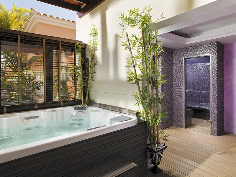 Outdoor jacuzzi with bamboo plants near a steam room.