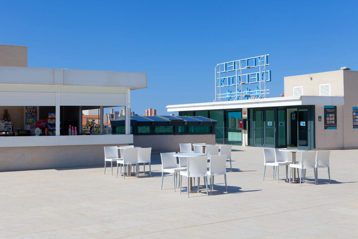 Terraza con mesas y sillas blancas bajo un cielo despejado.