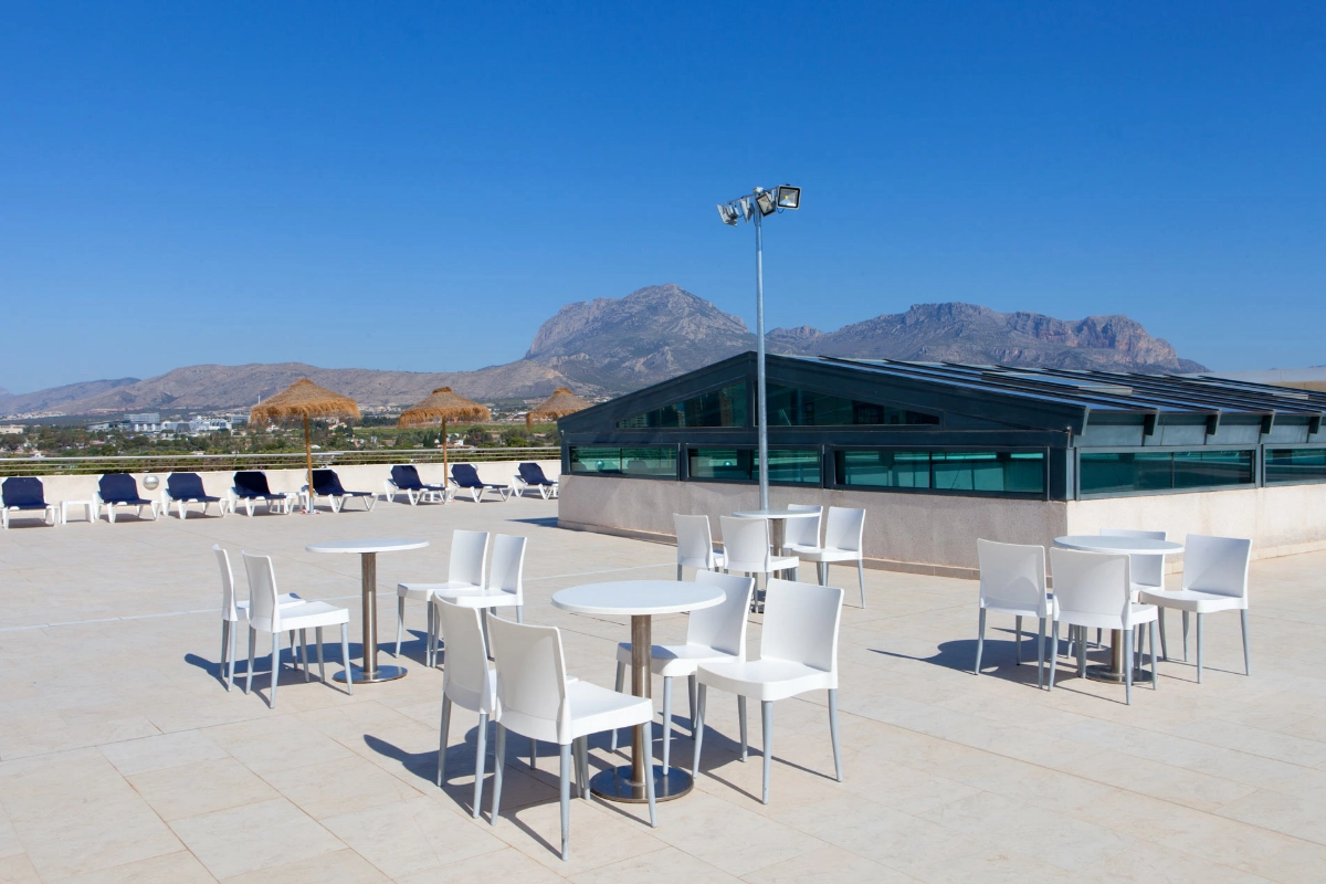 Terraza vac&iacute;a con sillas y mesas blancas, monta&ntilde;as al fondo.