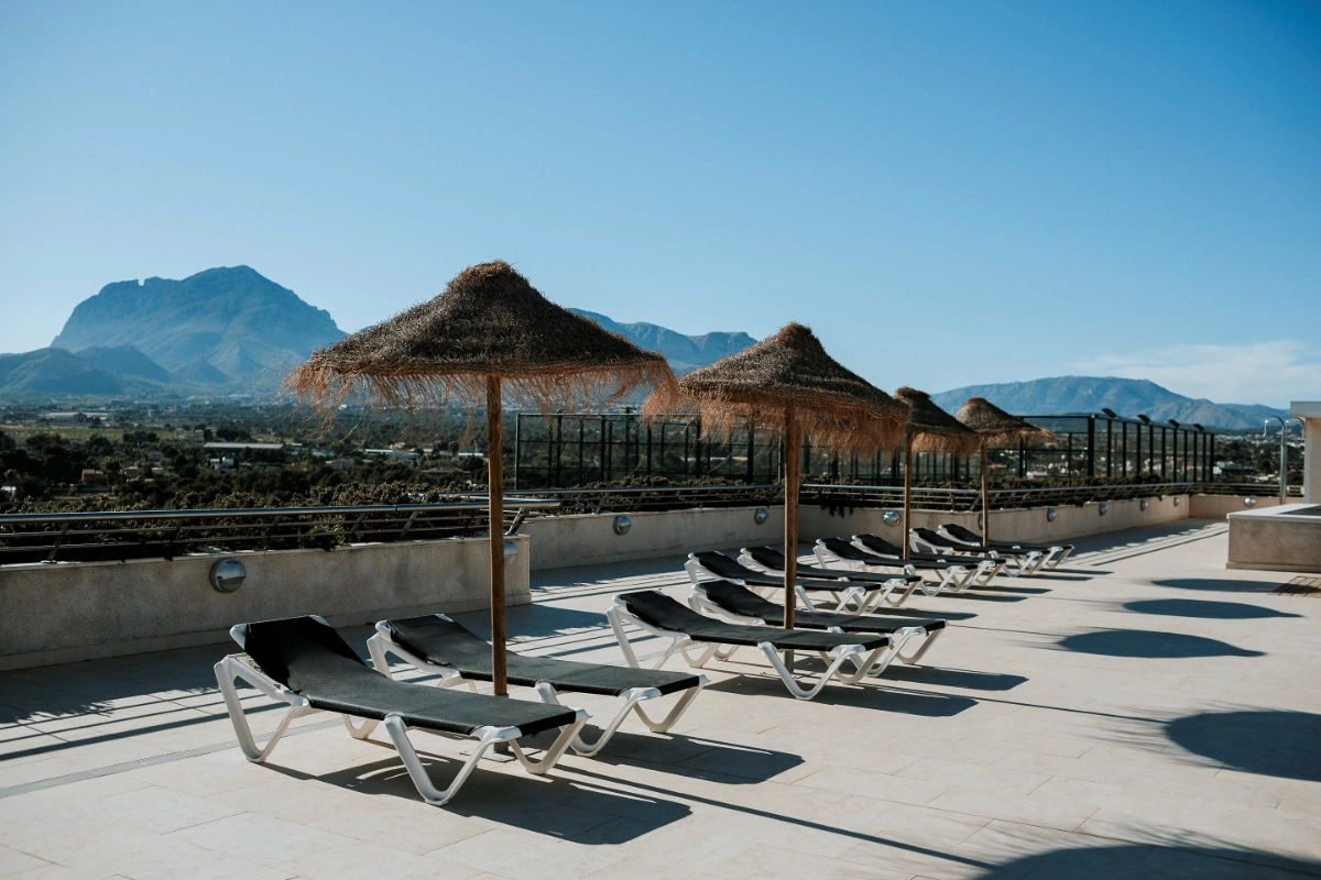 Terraza con tumbonas y sombrillas frente a monta&ntilde;as.