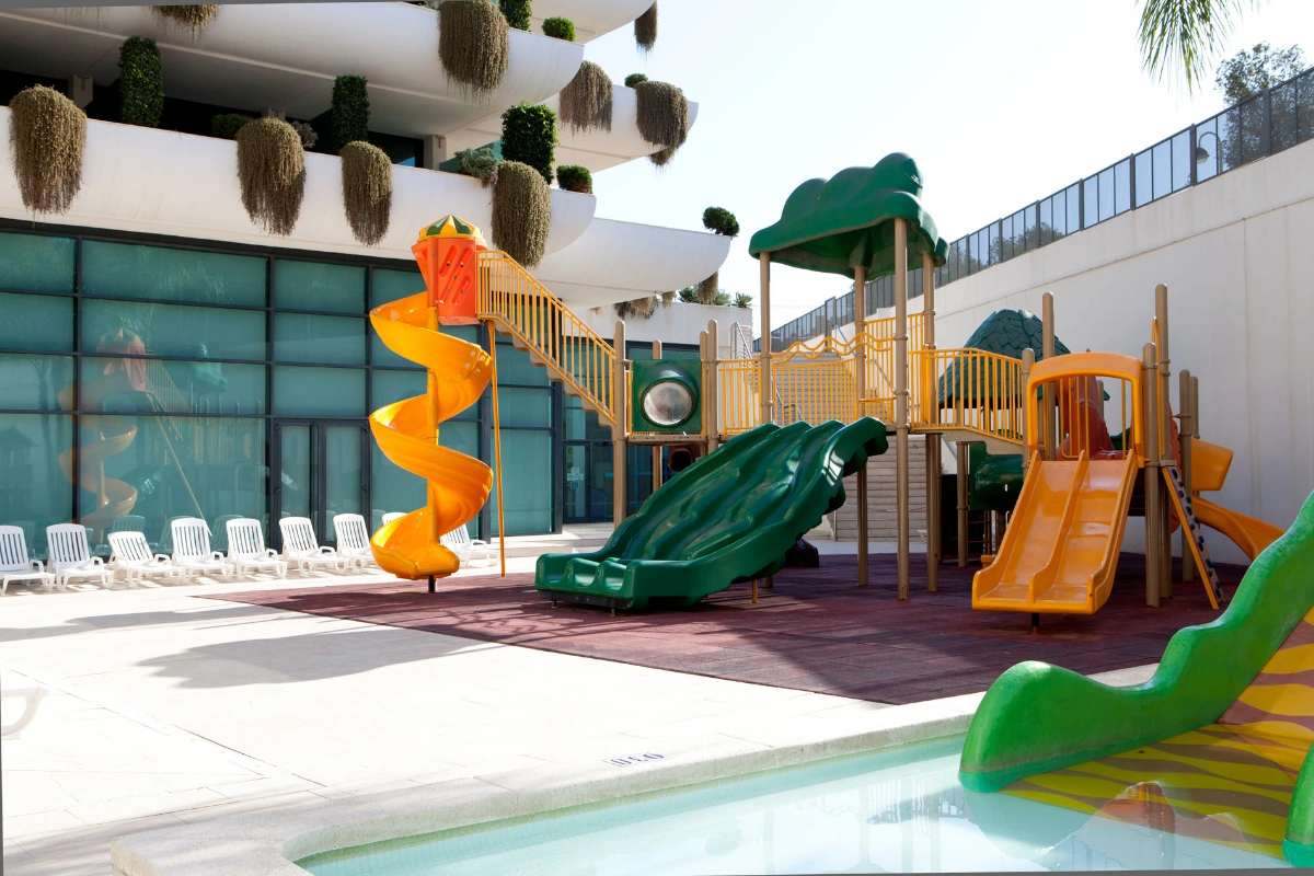 &Aacute;rea de juegos con toboganes coloridos junto a piscina en hotel.