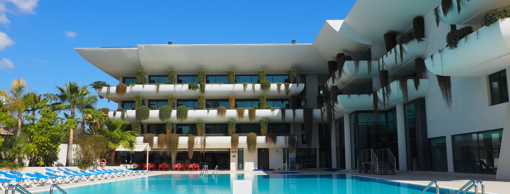 Edificio moderno con balcones y piscina rodeada de palmeras.