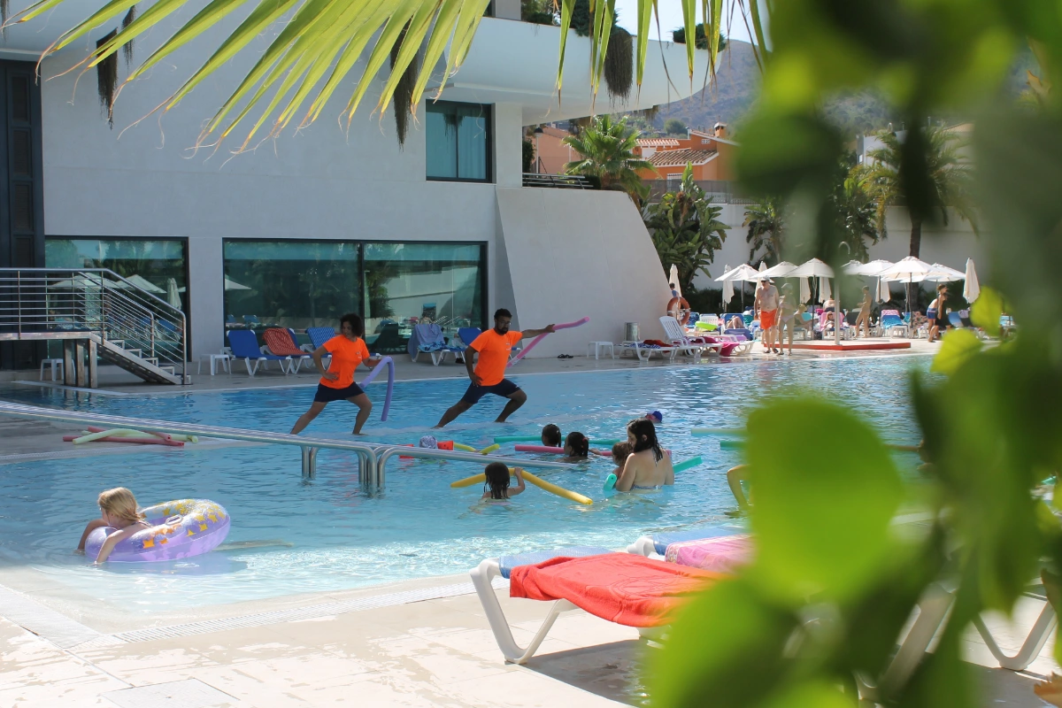 Personas disfrutando en una piscina junto a instructores en un d&iacute;a soleado.