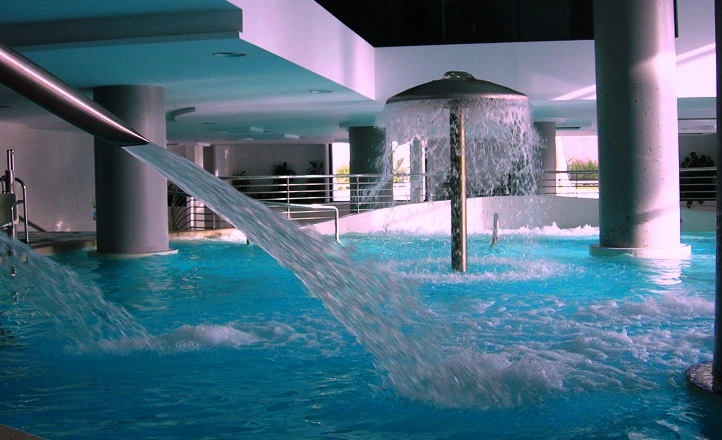 Piscina cubierta con fuentes de agua en un ambiente moderno y luminoso.