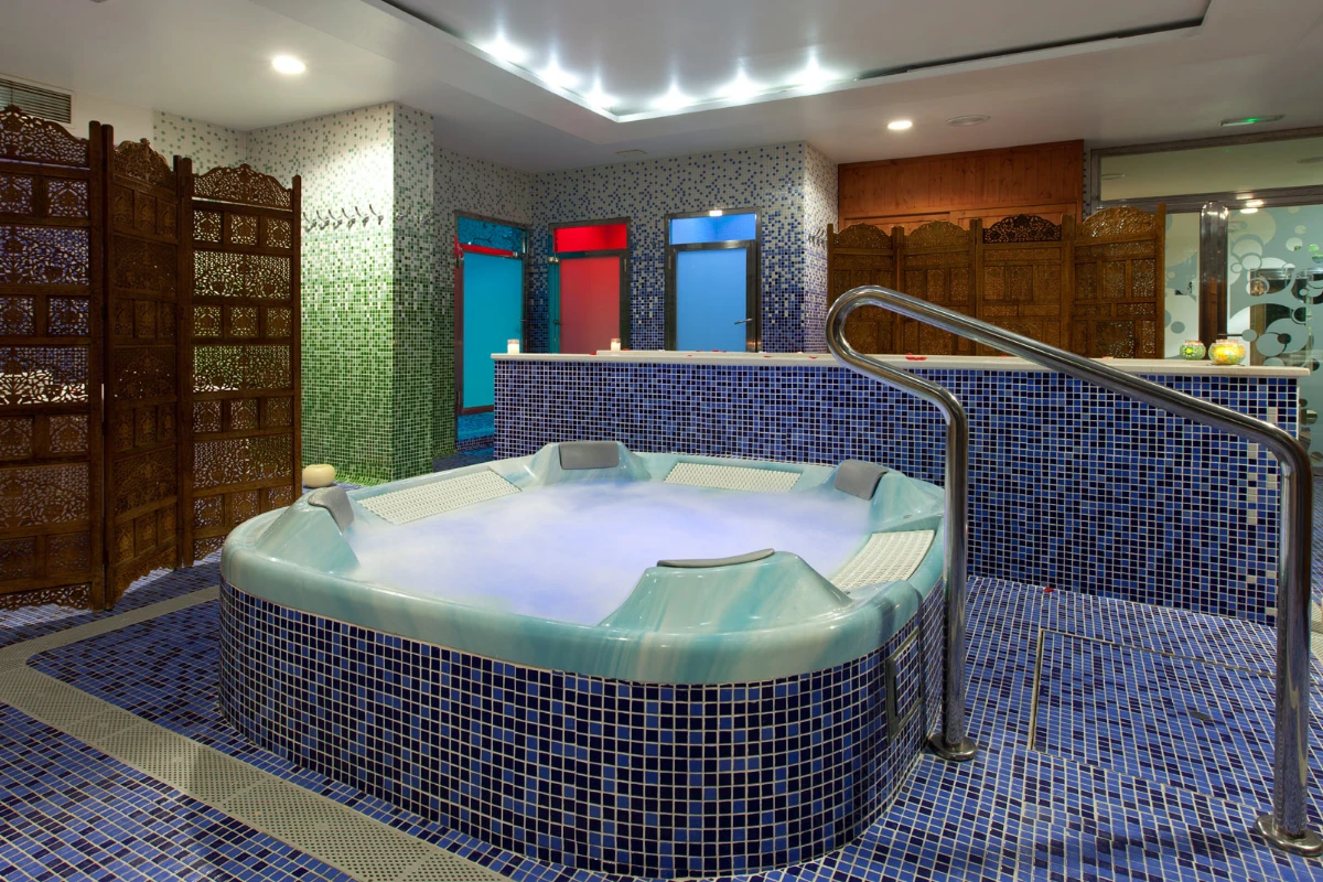 Jacuzzi rodeado de mosaicos azules y paneles decorativos de madera.