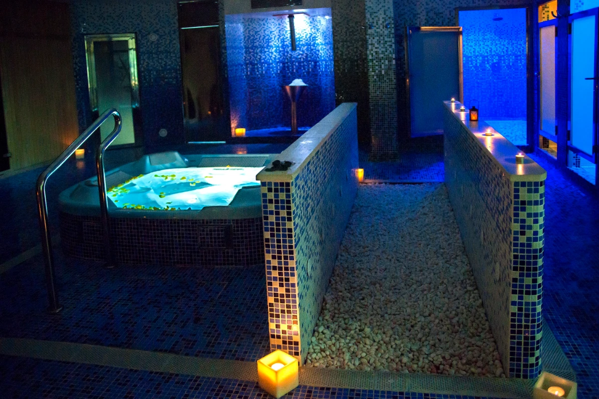 Spa iluminado con velas, jacuzzi y pasillo de mosaicos azules.