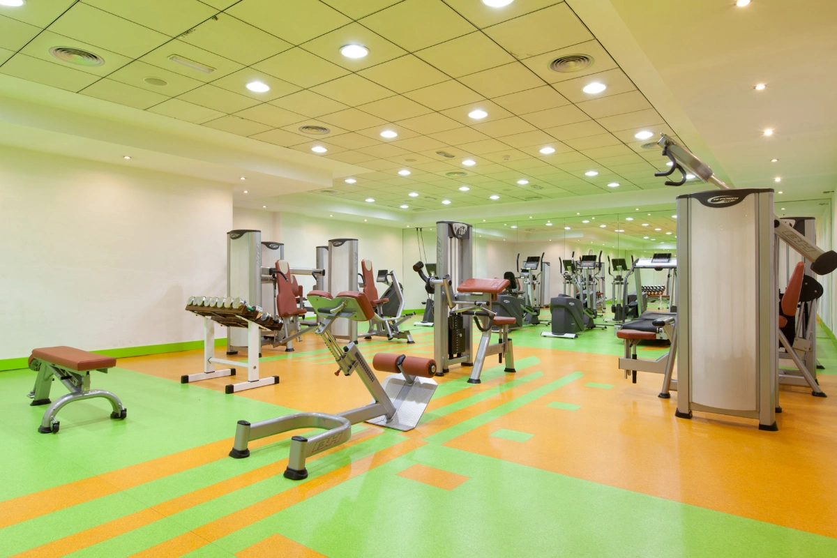 Gimnasio con m&aacute;quinas de ejercicio y suelo de colores verde y naranja.