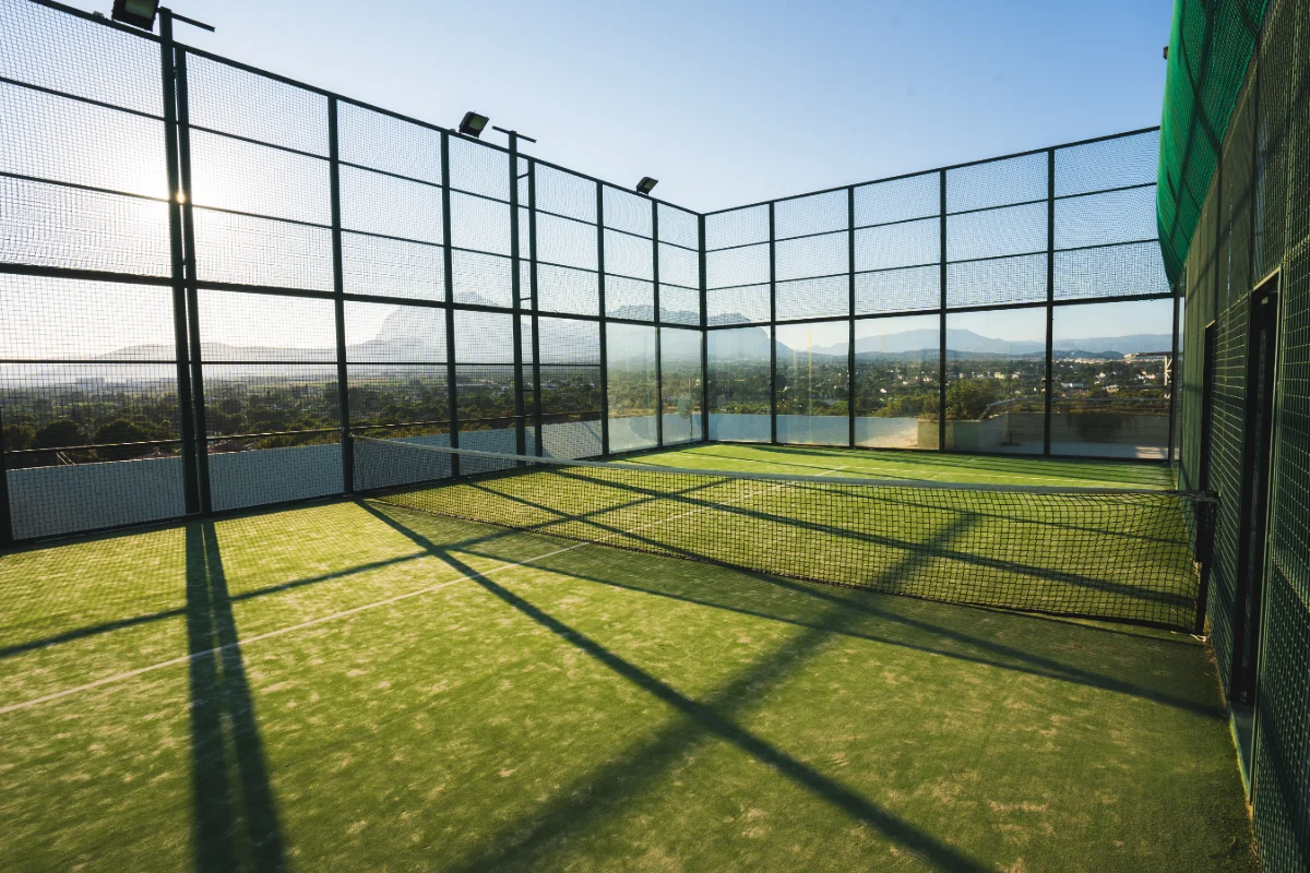 Cancha de p&aacute;del vac&iacute;a con red y fondo monta&ntilde;oso al atardecer.