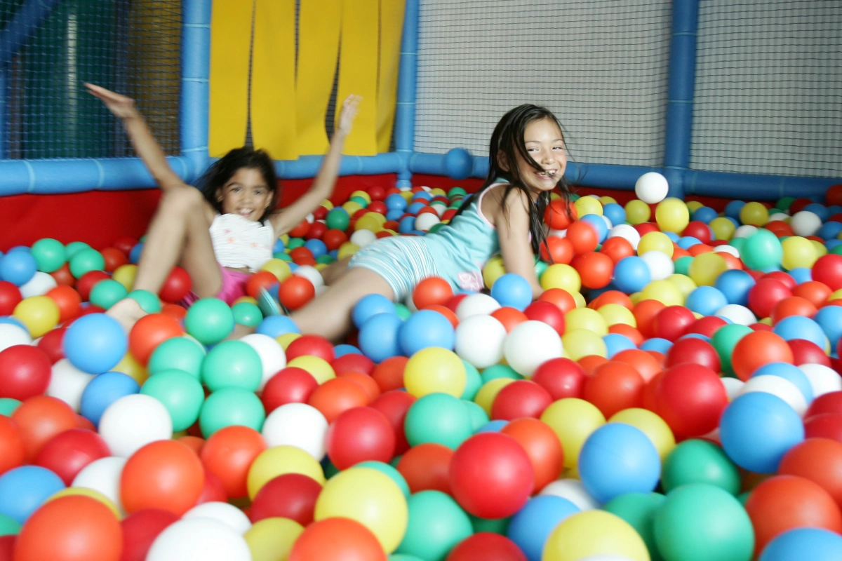 Ni&ntilde;as jugando felices en una piscina de pelotas de colores.