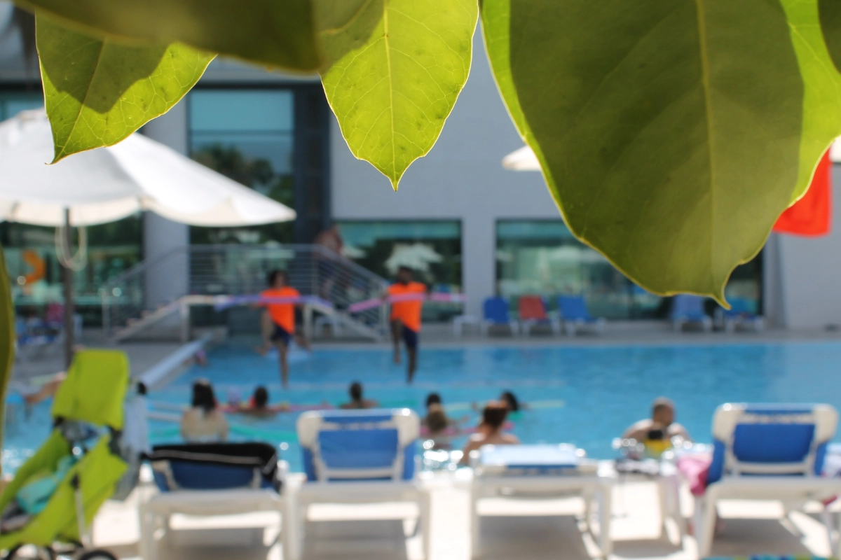 Hojas verdes sobre una piscina con personas y sillas junto al agua.
