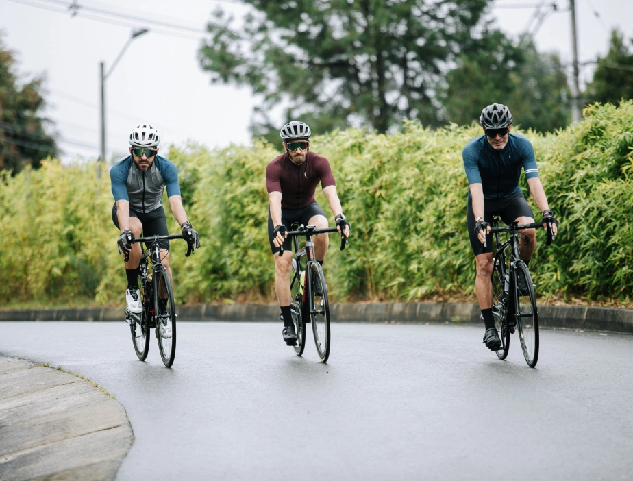 Tres ciclistas en una curva de carretera rodeados de vegetaci&oacute;n.