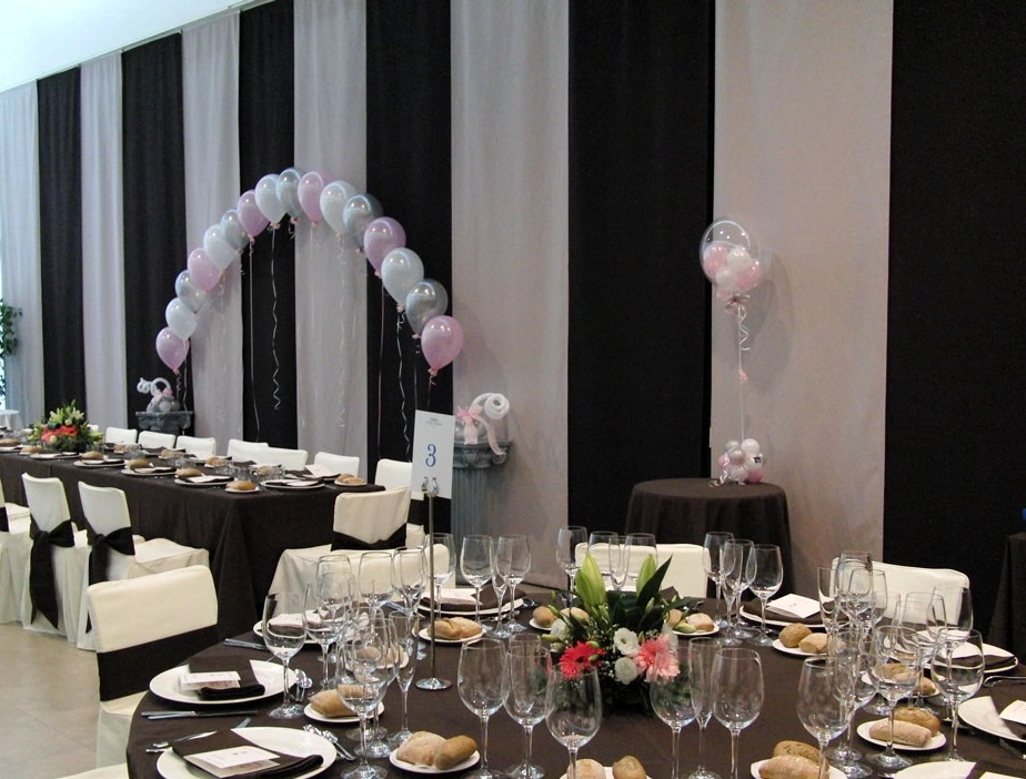 Sal&oacute;n de eventos con mesas decoradas y arco de globos.