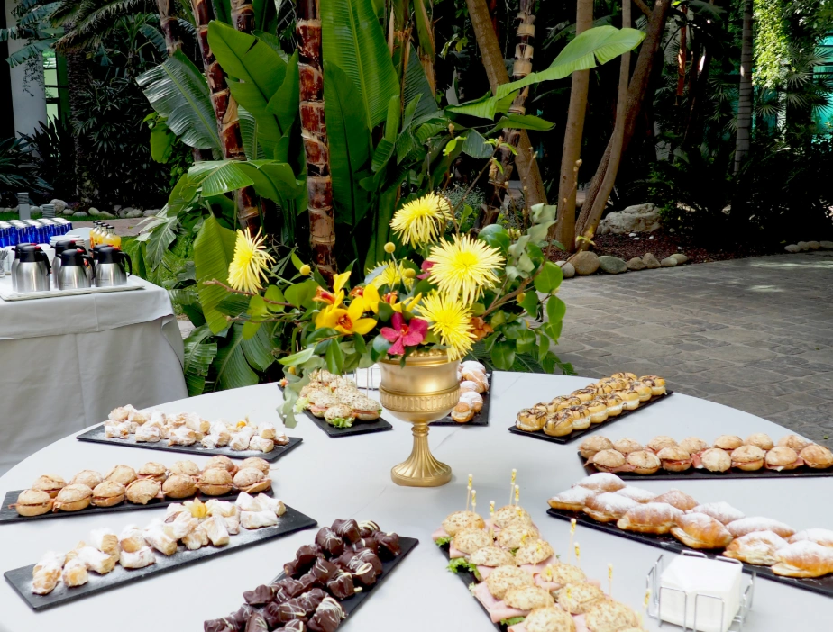 Mesa con postres y flores en un entorno tropical.