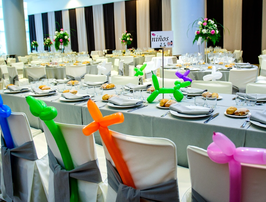 Mesa con globos de colores, platos y sillas; secci&oacute;n de ni&ntilde;os.