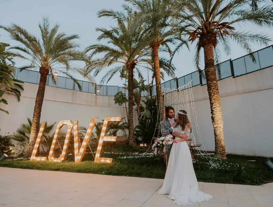 Pareja de reci&eacute;n casados en jard&iacute;n con letras iluminadas que dicen "LOVE".