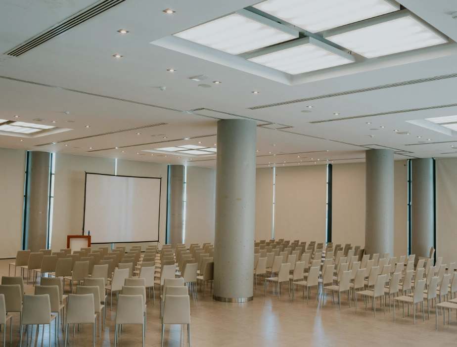 Sala de conferencias vac&iacute;a con filas de sillas y una pantalla grande.