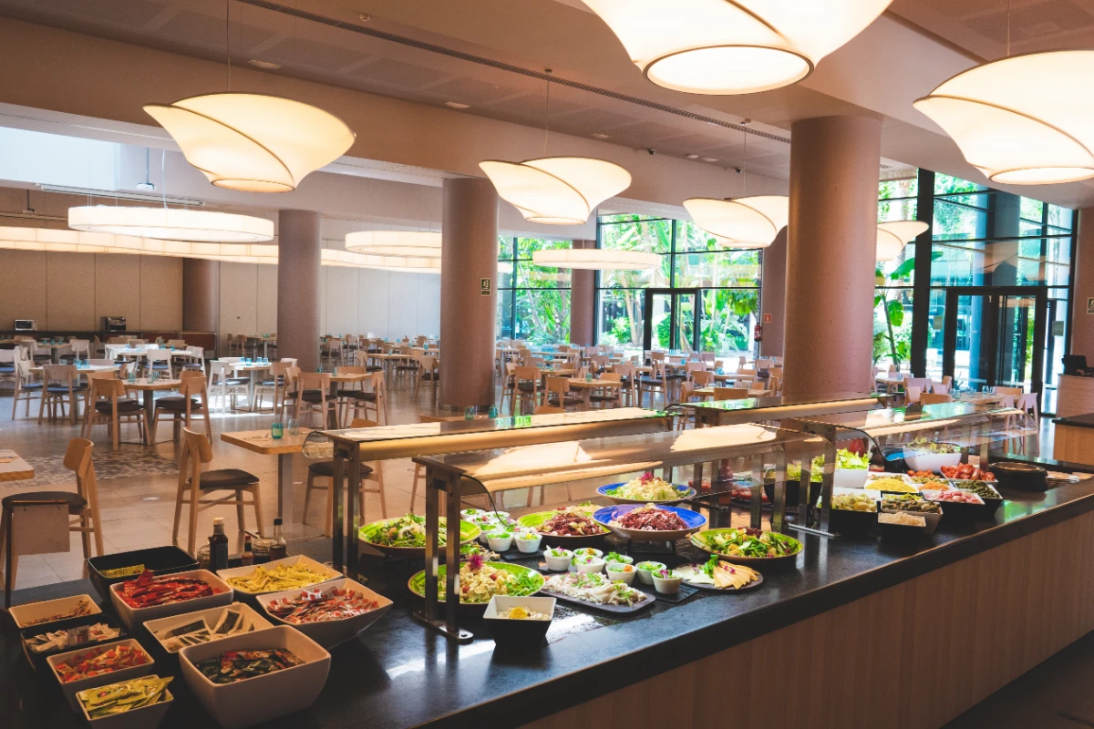 Buffet de ensaladas en un amplio comedor con l&aacute;mparas modernas.
