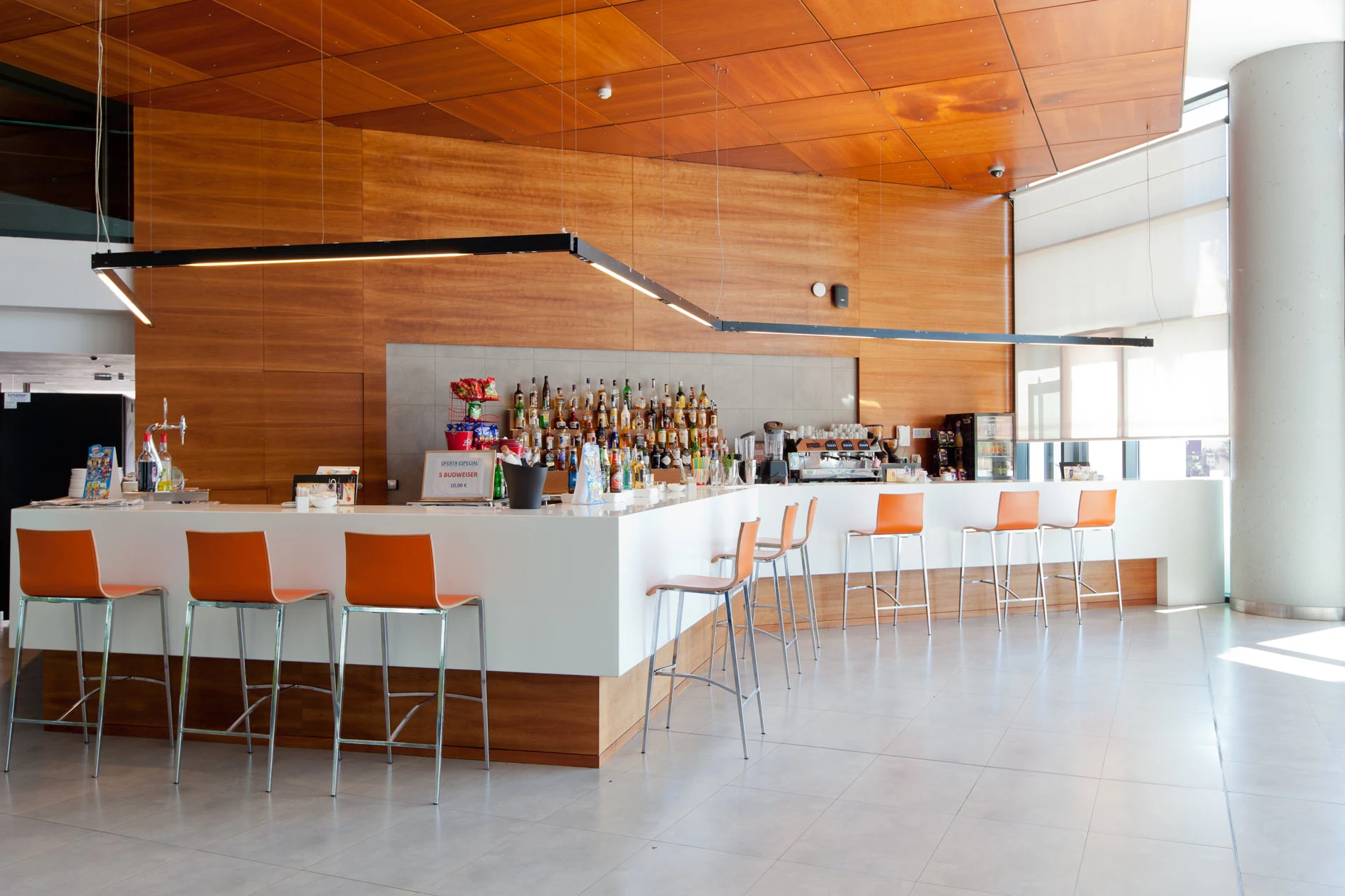 Bar moderno con sillas naranjas y botellas de licor en el fondo.