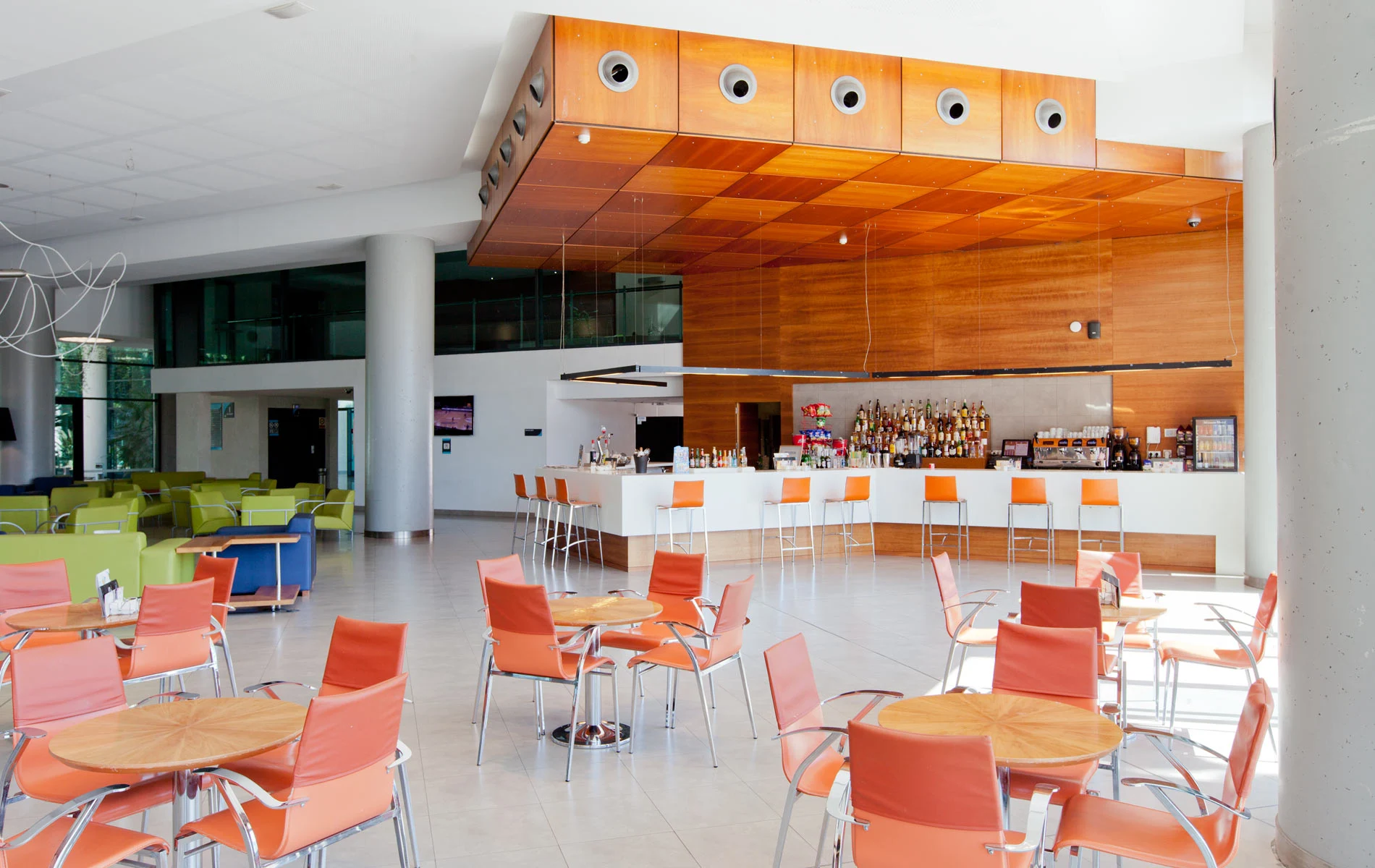 Cafeter&iacute;a moderna con sillas naranjas y barra de bar iluminada.