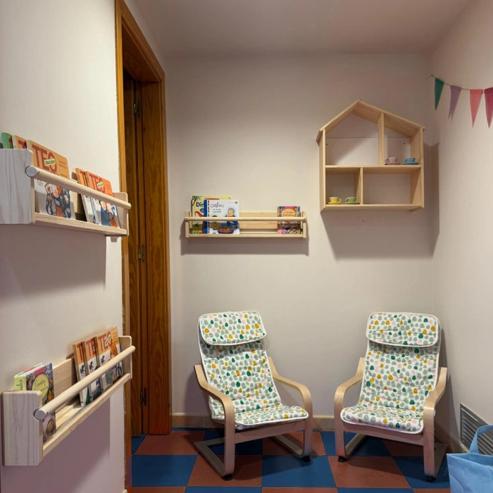 Sala infantil con sillas, libros y estantes decorativos en la pared.