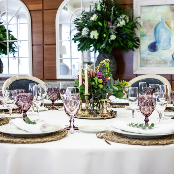Mesa elegante con copas moradas y arreglo floral en restaurante lujoso.