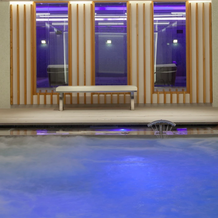 Piscina iluminada en interior con banco y ventanas.