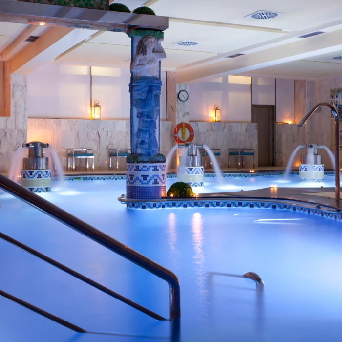 Piscina iluminada en interior con esculturas y fuentes decorativas.