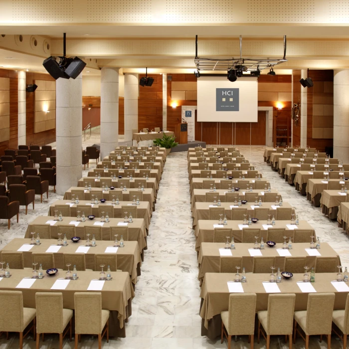 Sala de conferencias preparada con mesas y sillas en filas, lista para un evento.