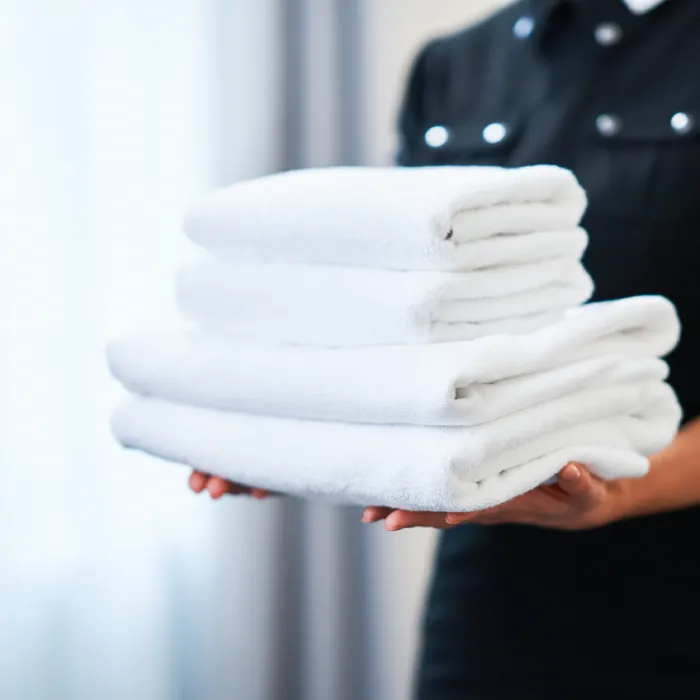 Manos sostienen toallas blancas dobladas en un entorno de limpieza.