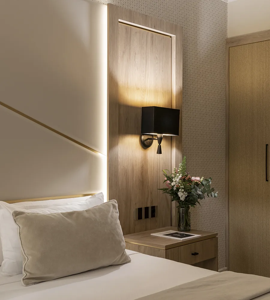 Habitaci&oacute;n moderna con cama, l&aacute;mpara negra y flores sobre el mueble.