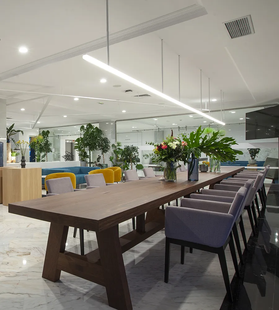 Sala moderna con mesa larga, sillas, plantas y flores decorativas.