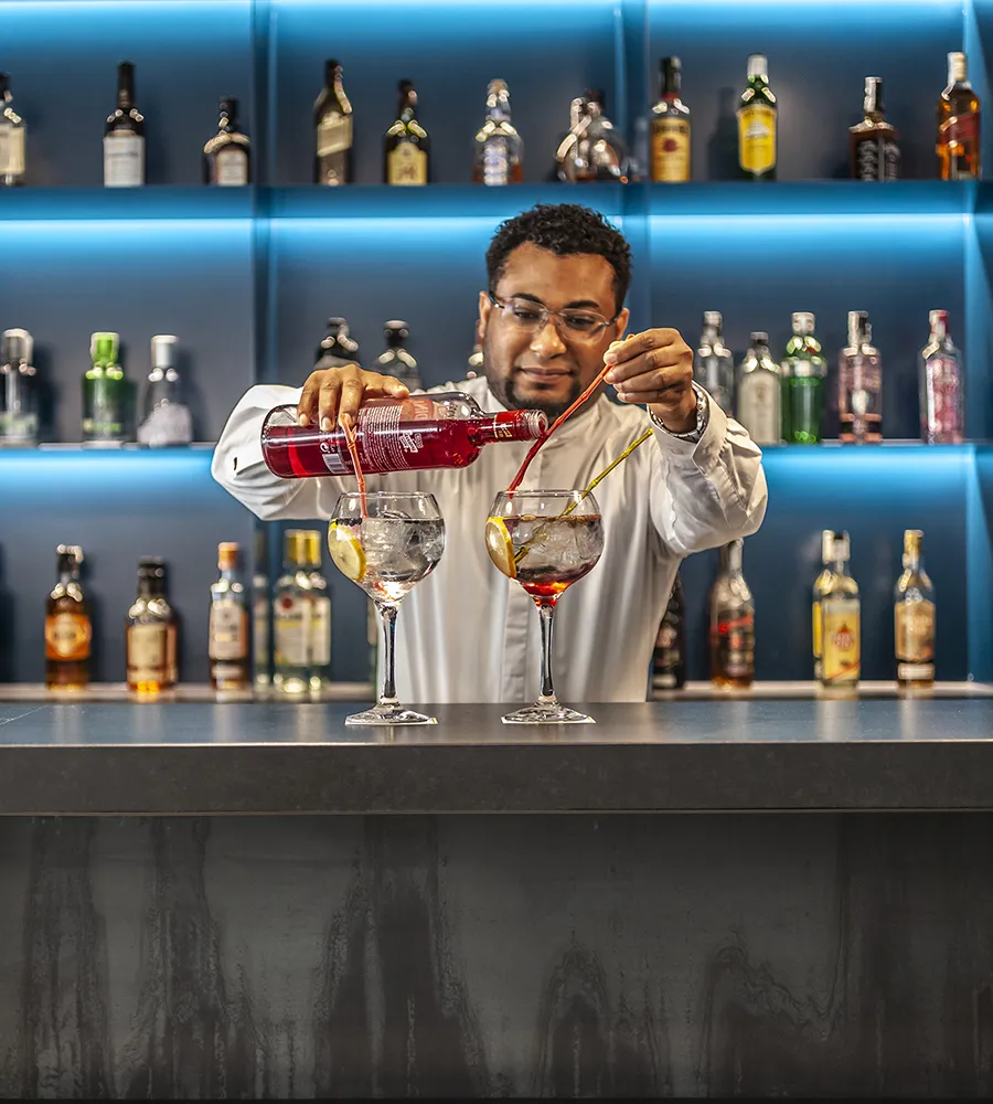 Bartender sirviendo bebidas en la barra con botellas al fondo.