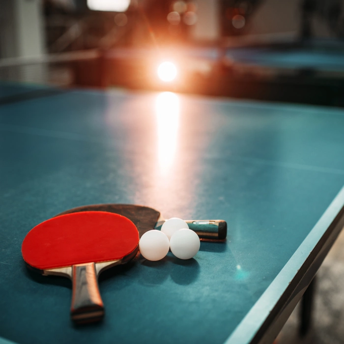 Mesa de ping pong con paleta y pelotas blancas al atardecer.