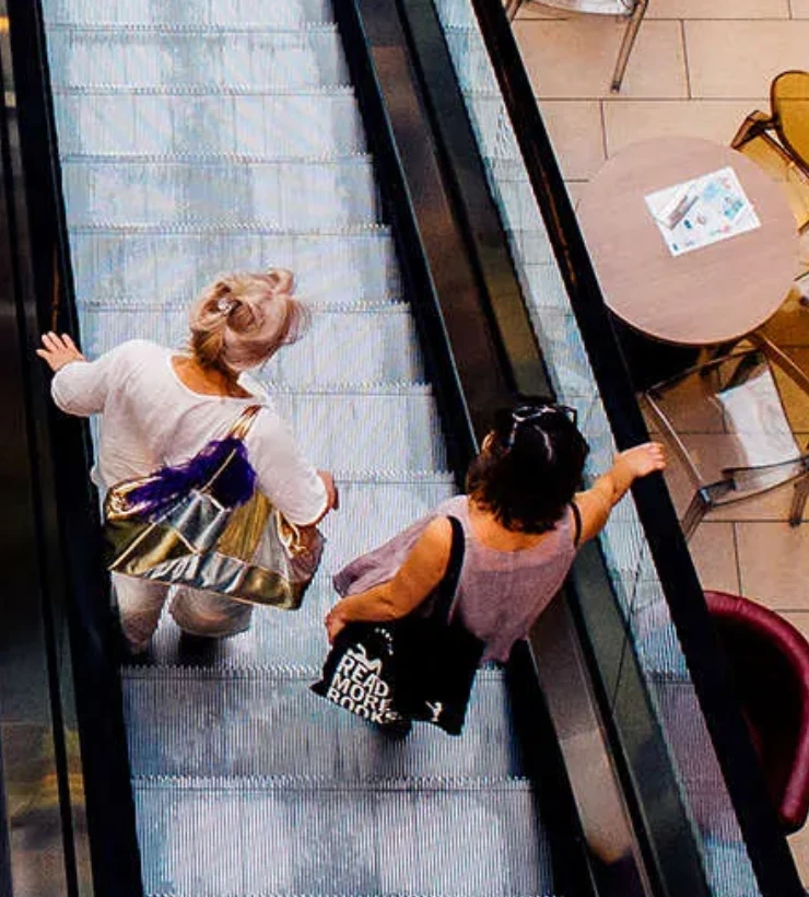 Dos personas bajando por una escalera mec&aacute;nica en un centro comercial.