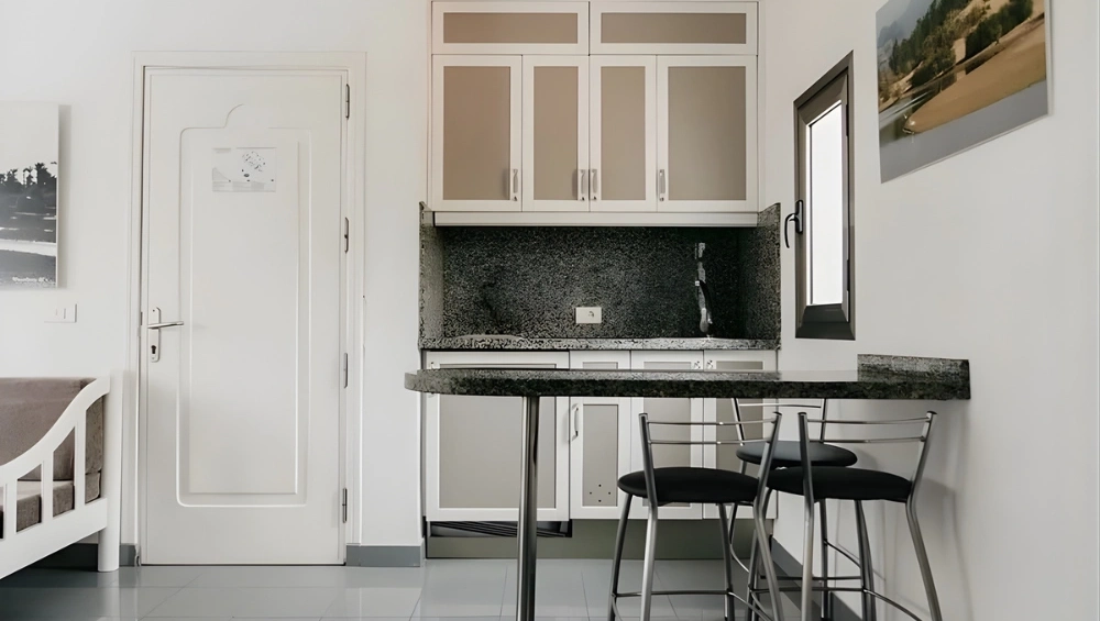 Cocina minimalista con barra y sillas, puertas blancas y ventana peque&ntilde;a.