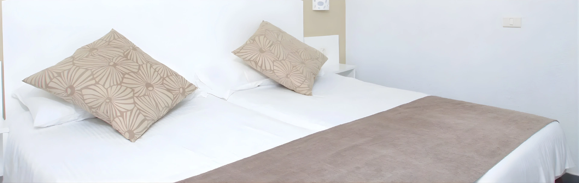 Cama doble con cojines decorativos y manta marr&oacute;n en habitaci&oacute;n blanca.