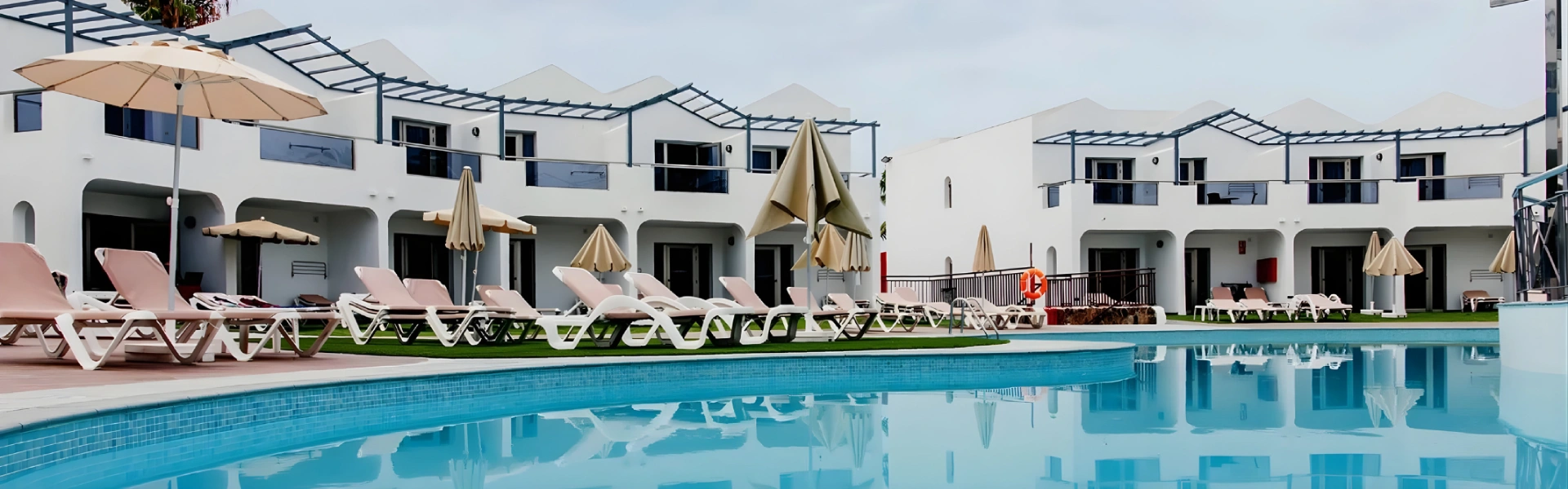 Piscina frente a villas blancas con tumbonas y sombrillas.