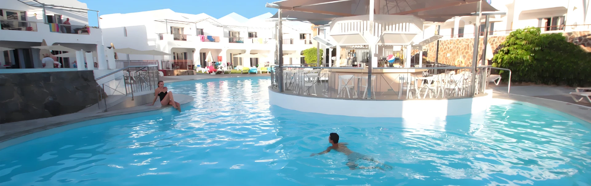 Piscina con bar en el centro y personas disfrutando del agua.