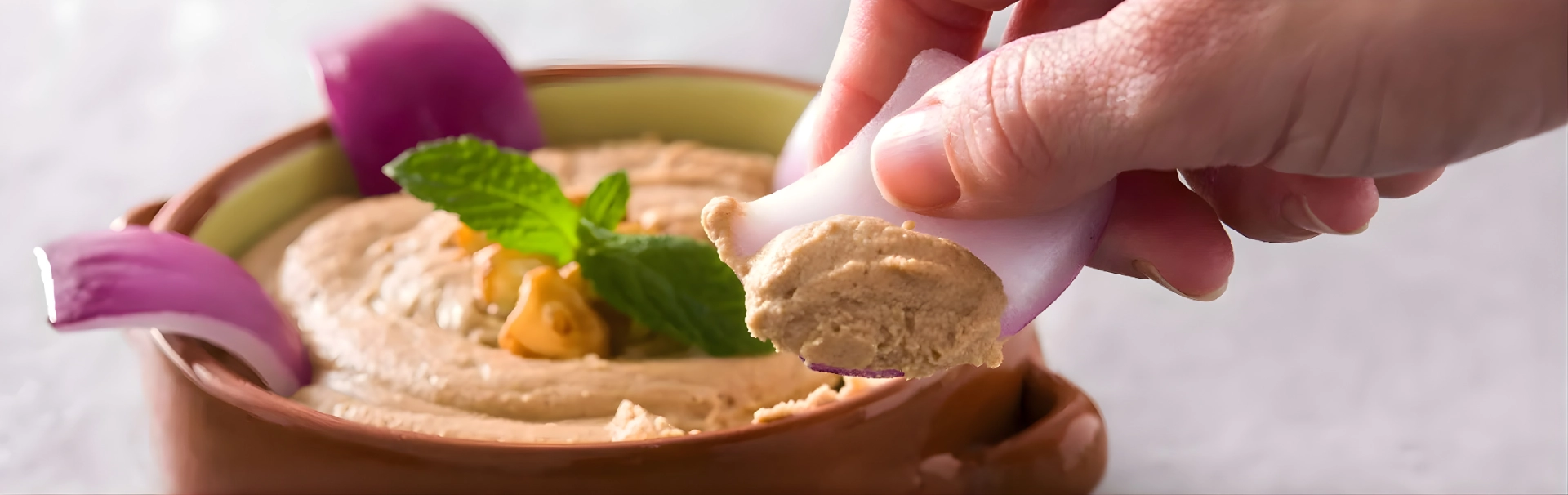 Persona untando hummus en rodaja de cebolla roja.