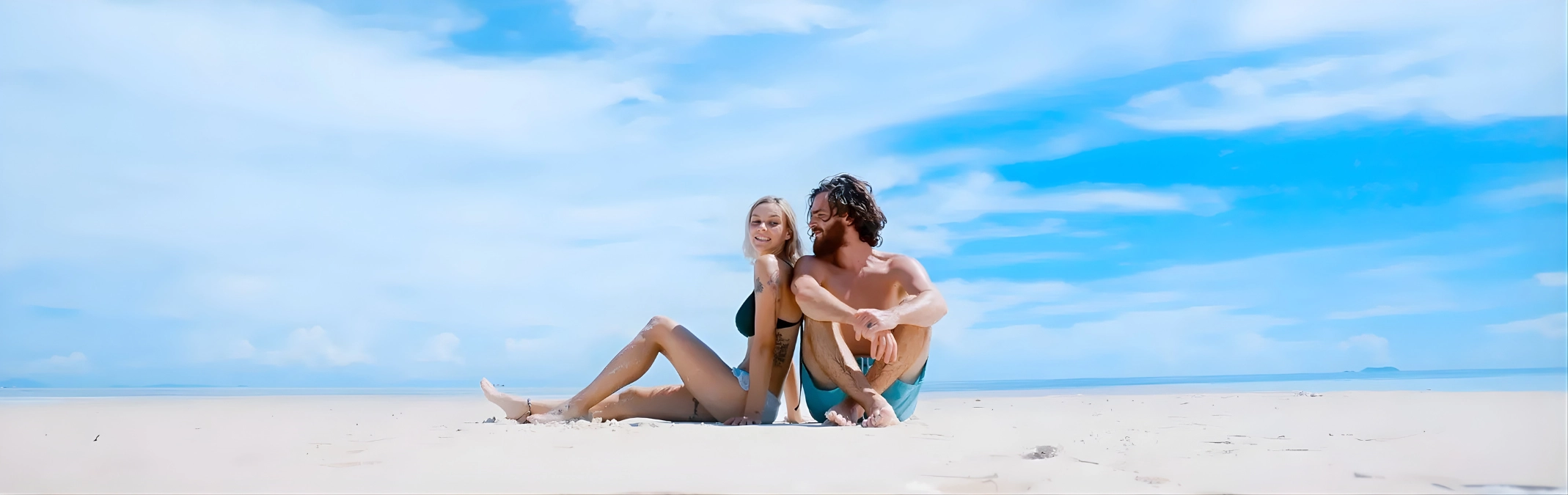 Pareja disfrutando en la playa bajo un cielo azul y despejado.