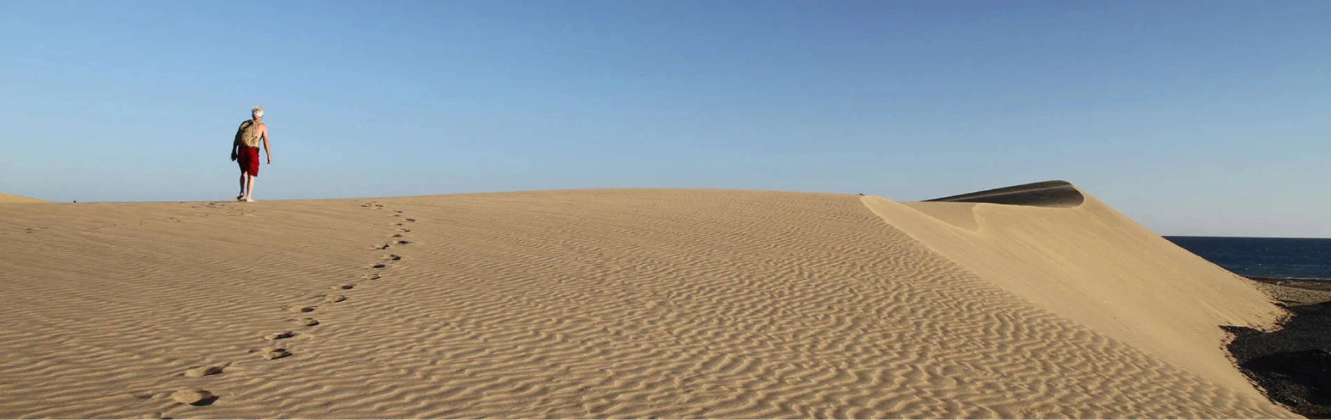 Persona caminando sobre una duna de arena con huellas hacia el horizonte.