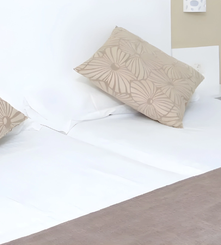 Cama con almohada de dise&ntilde;o floral beige sobre s&aacute;banas blancas.