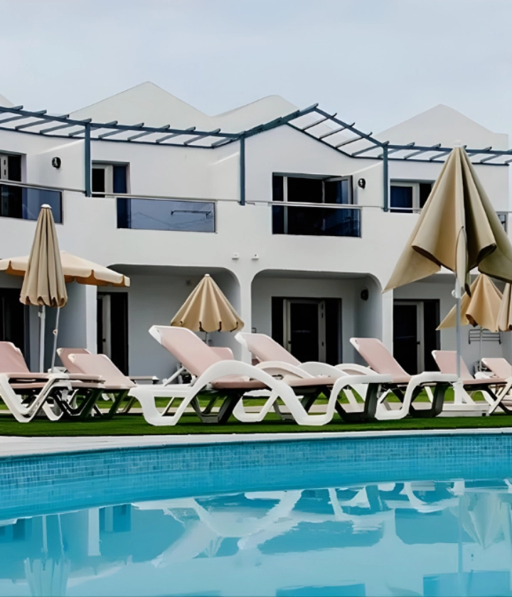 Piscina con tumbonas y sombrillas frente a un edificio moderno.