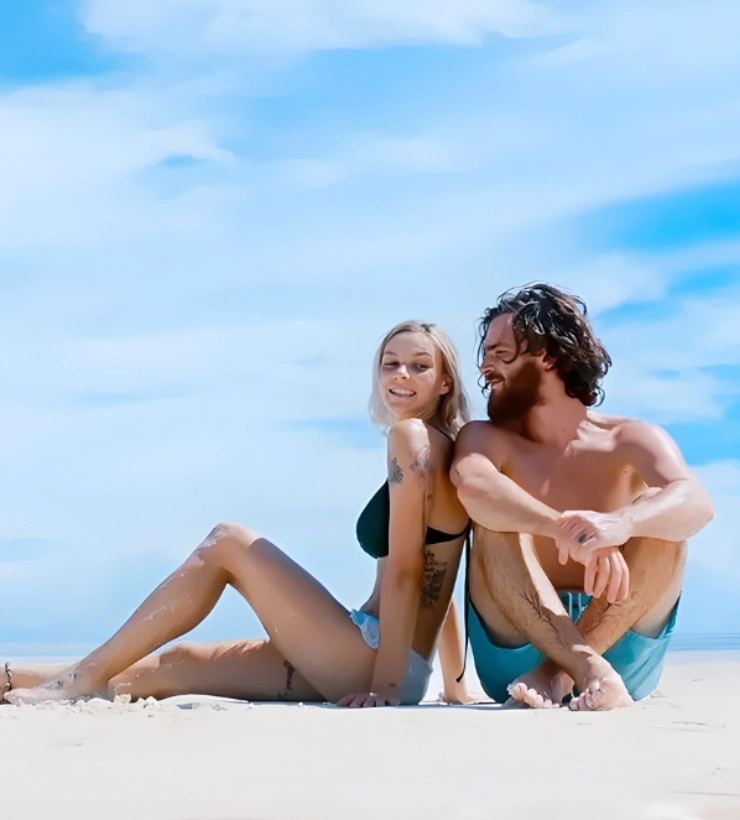 Pareja sentada en la playa, felices bajo el cielo azul.
