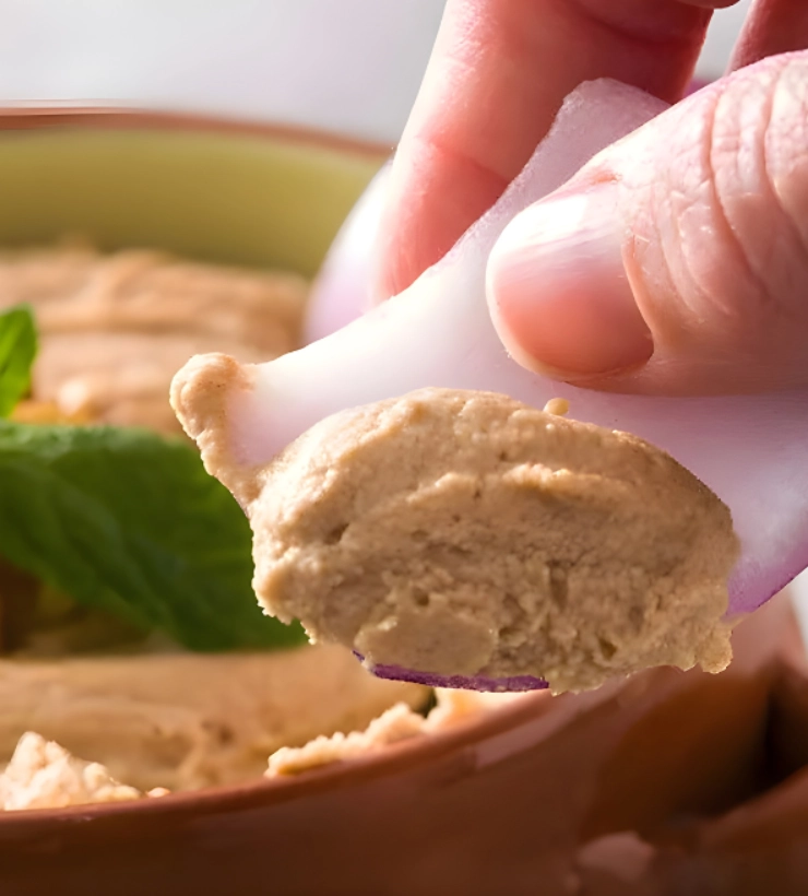 Dedo sosteniendo un trozo de cebolla con hummus.