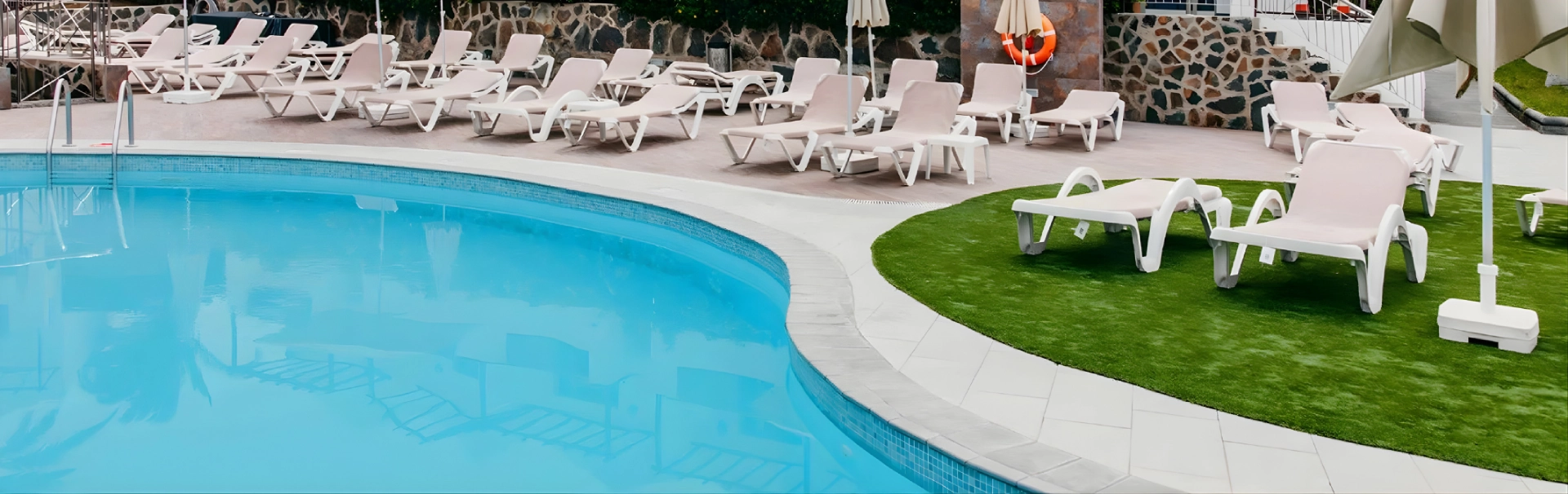 Piscina al aire libre con tumbonas blancas y sombrillas alrededor.