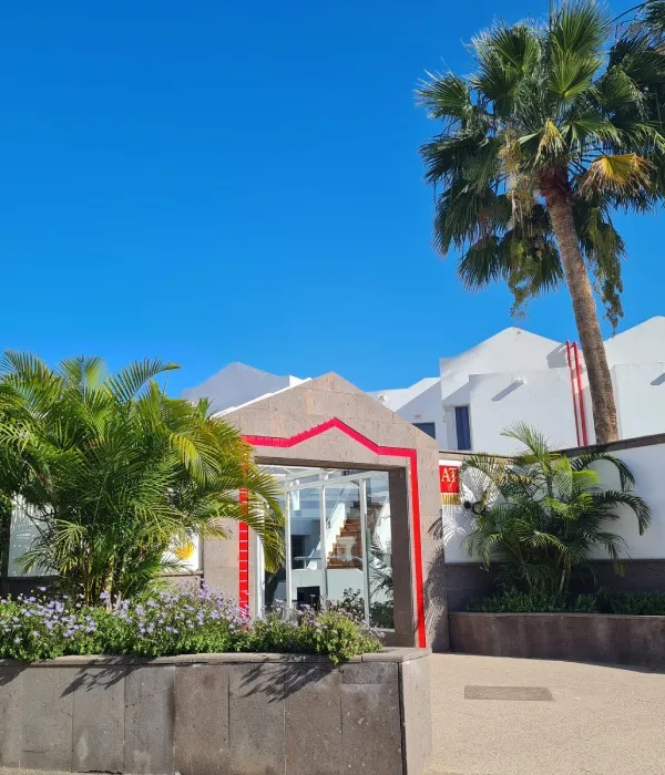 Edificio moderno con decoraci&oacute;n roja, plantas y palmera, cielo despejado.