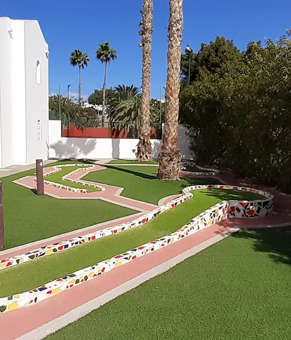 Mini golf con c&eacute;sped artificial y bordes coloridos, palmeras al fondo.